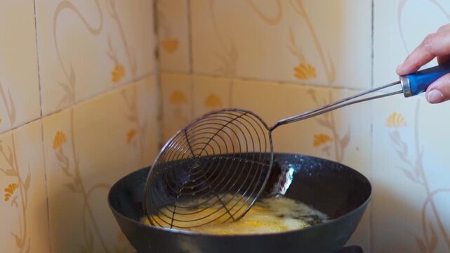 Closeup shot of Indian woman deep frying snacks in hot oil in kitchen at home. Indian housewife preparing food at home. Homemade fried snakes. 