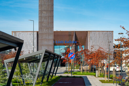 Modern Ł&oacute;dź Kaliska railway station building with copper facade, covered bicycle parking and urban infrastructure at the main entrance, autumn scenery with trees and blue sky in Ł&oacute;dź.