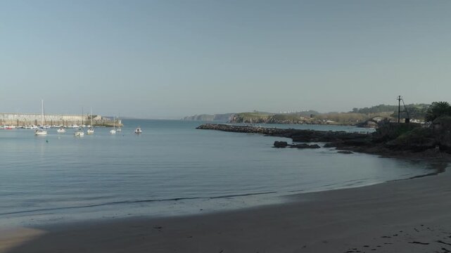 Scenic wide view of a sandy beach and rocky Atlantic coastline in Cand&aacute;s, Asturias, Spain. People walk along the shore while gentle waves reach the beach under clear skies.