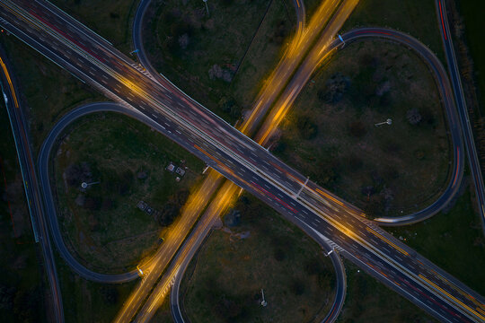 Aerial view of the cloverleaf interchange glows with golden trails of light against the dark green landscape, Rome, Lazio, Italy.