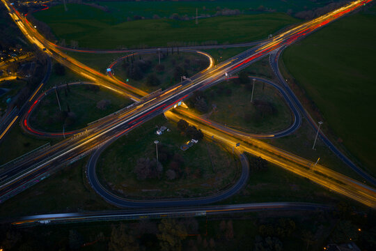 Aerial view of a cloverleaf interchange glows with streaks of light, cutting through the dark green landscape, Rome, Lazio, Italy.