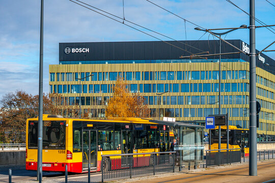 Yellow city bus at bus stop with modern Bosch and Beko office building background, public transport infrastructure, urban architecture with golden facade, sunny day cityscape, corporate headquarters, 