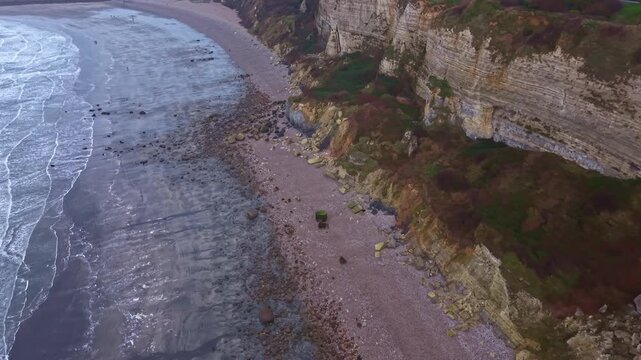 Waves crashing on the beach at the bottom of chalk cliffs on the Alabaster Coast, Plage de Saint-Jouin-Bruneval, Normandy, France. Aerial drone forward
