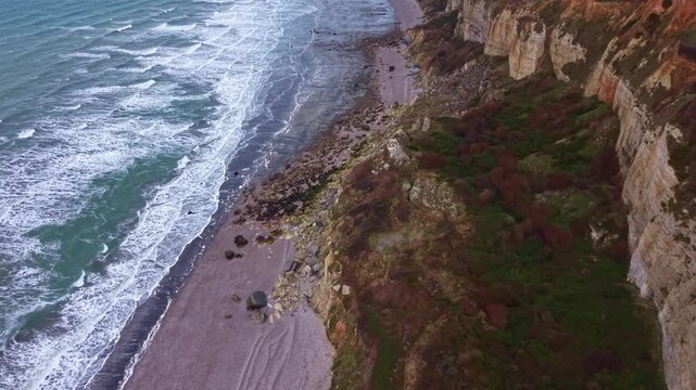 Waves crashing on the beach at the bottom of chalk cliffs on the Alabaster Coast, France. Aerial backward