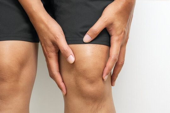 Hand holding injured left knee on white background with copy space for advertising use.
