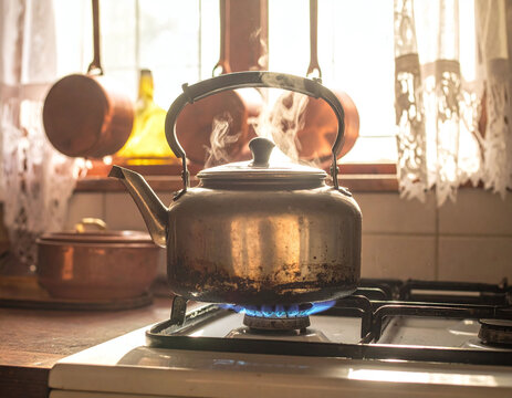 This vintage metal kettle boils over a blue gas flame in a warm, sunlit rustic kitchen. Evoking a sense of nostalgic comfort, its ideal for lifestyle, home, and culinary themes.