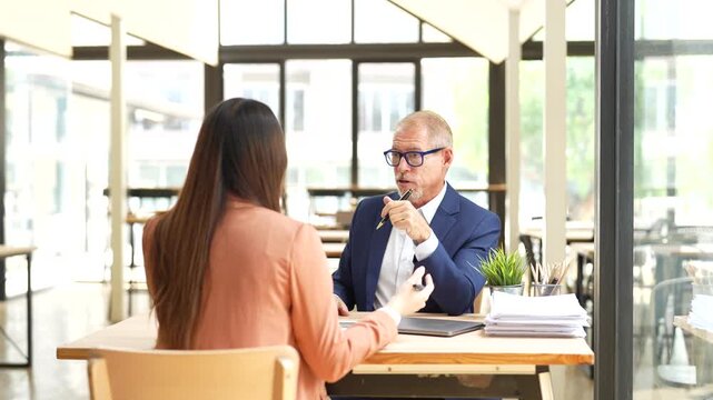 Senior manager interviewing a young female applicant for a job opening in a modern office, discussing her resume and professional experience during the hiring and recruitment process