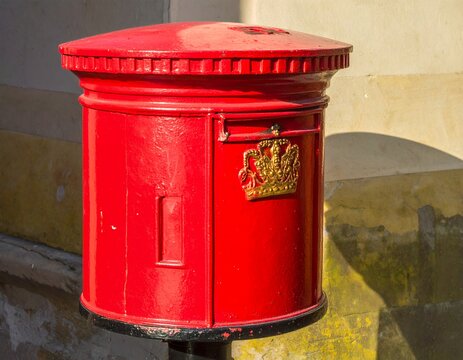 Vibrant Red British Post Box with Golden Royal Cypher in Sunlight.