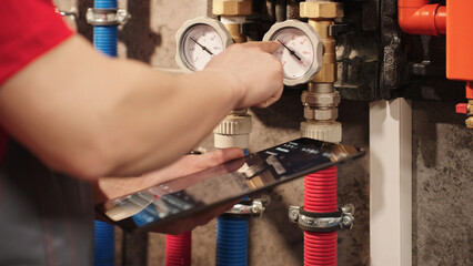 Technician Checking Heating System Gauges And Monitoring Boiler Data Using Digital Tablet In Utility Room. Residential HVAC Inspection And Plumbing Maintenance Diagnostics Concept.
