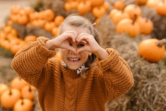 Child making heart gesture in pumpkin patch during autumn harvest