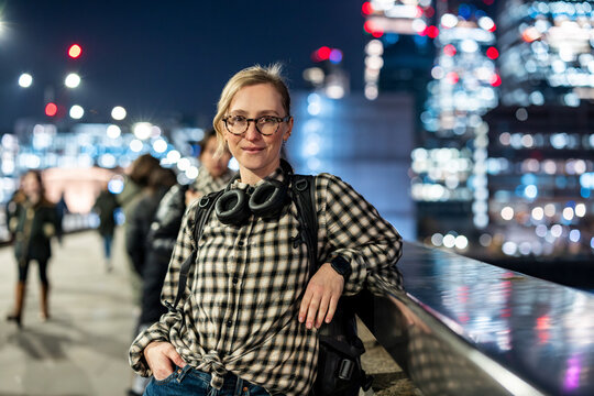 Confident woman with headphones on London bridge at night