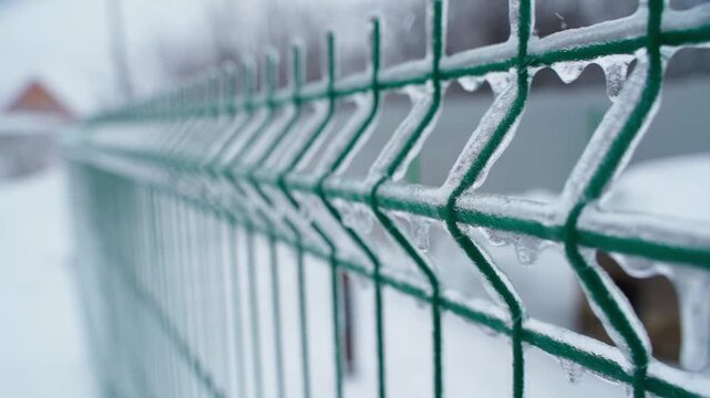 Smooth camera movement along green mesh fence covered with ice after freezing rain close-up