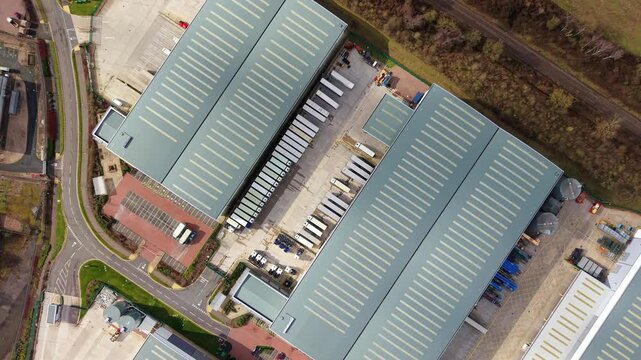 Aerial view of industrial buildings with rows of parked trucks, creating a geometric pattern of grey roofs and white trailers, Birmingham, United Kingdom.
