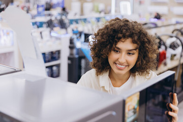Happy woman shopping, choosing new home appliance at electronics store, looking at microwave oven...