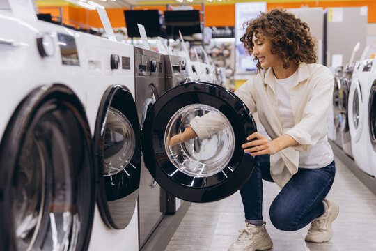 Woman shopping for new washing machine in appliance store, inspecting features for laundry and home