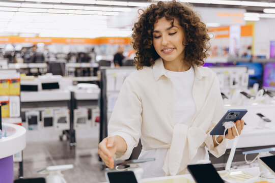 Woman choosing a new smartphone in an electronics store, shopping for modern communication technology