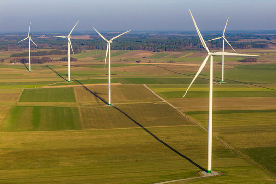 Aerial view of wind turbines casting long shadows across the patchwork fields, a symphony of green and brown under a clear sky, Stawiski, Podlaskie Voivodeship, Poland.