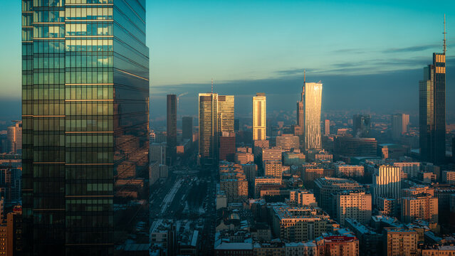 Warsaw, Poland - 06 February 2023: Aerial view of a modern cityscape with towering skyscrapers gleaming in the sunlight, casting long shadows across the bustling city below.