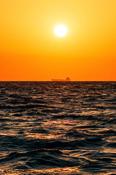 Cargo ship silhouette on ocean horizon during golden sunset