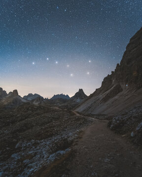 View of a starlit sky hangs above a rugged mountain path, the cool moonlight casting long shadows across the rocky landscape, Auronzo di Cadore, Veneto, Italy.