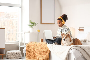 Teenage African-American girl with Corgi dog using laptop in bedroom