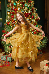 Girl in yellow dress smiles near Christmas tree with gifts