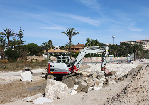 Obra en playa con excavadora y pala con piedras en el suelo y palmeras