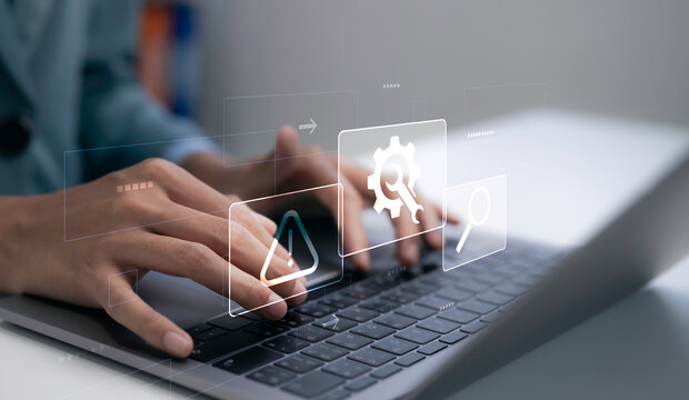 Business professional typing on laptop with warning alert and system maintenance icons. IT support, cybersecurity monitoring, troubleshooting and digital technology management