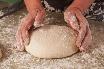 Hands shaping raw dough covered in flour on a floured surface, preparing for baking