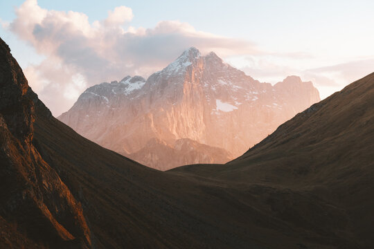 View of the majestic, snow-kissed mountain peak bathed in the warm glow of the setting sun, framed by the dark, sloping hillsides, San Vito di Cadore, Veneto, Italy.