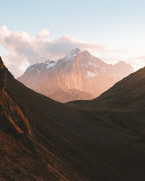 View of a majestic mountain peak kissed by the warm glow of the setting sun, nestled between shadowy valleys under a soft, pastel sky, San Vito di Cadore, Veneto, Italy.