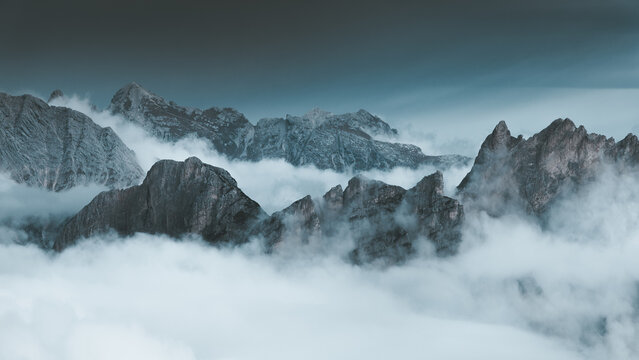 View of jagged peaks piercing through a sea of ethereal clouds, where nature's raw beauty meets serene tranquility, San Vito di Cadore, Veneto, Italy.