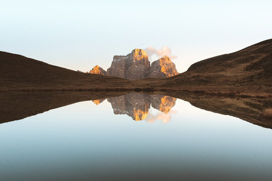 View of striking mountain peaks kissed by golden sunlight, mirrored in the tranquil lake's embrace, reflecting serenity and awe, San Vito di Cadore, Veneto, Italy.