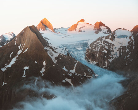 View of imposing, snow-capped peaks kissed by the warm glow of sunrise, with mist curling at their base, a breathtaking landscape, Obergoms VS, Switzerland.