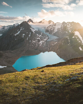 View of a pristine turquoise lake nestled amidst rugged, snow-capped mountains under a radiant sun, creating a striking contrast between the alpine landscape, Obergoms, Switzerland.