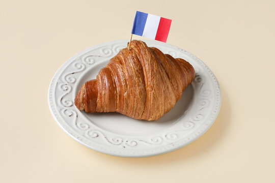 Plate with croissant and French flag on beige background