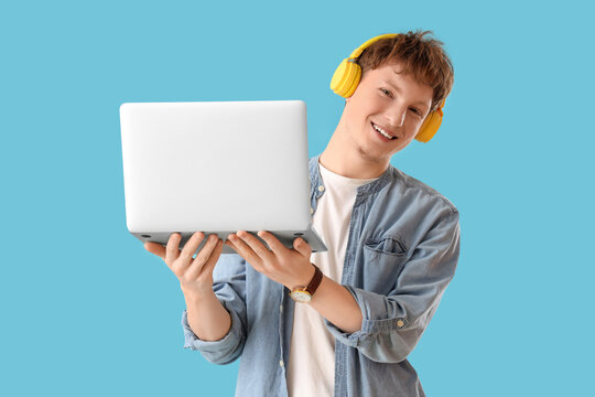 Young man in headphones with laptop on blue background