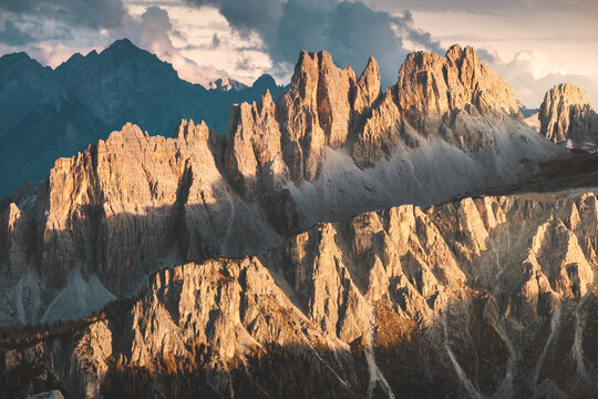View of jagged peaks catching the golden light under a dramatic sky, casting long shadows across the majestic landscape, Cortina d'Ampezzo, Veneto, Italy.