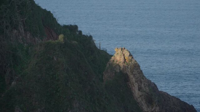 Dramatic rocky cliff covered with green vegetation overlooking the Atlantic Ocean near Cand&aacute;s in Asturias, Spain. Scenic coastal landscape with rugged cliffs and calm blue sea along northern Spain.