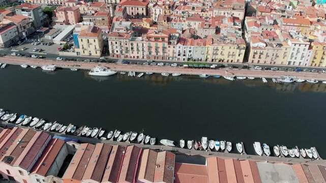 Aerial drone pan over the Temo River flowing through the colorful town of Bosa on the west coast of Sardinia, Italy, with picturesque riverside houses and a scenic Mediterranean landscape