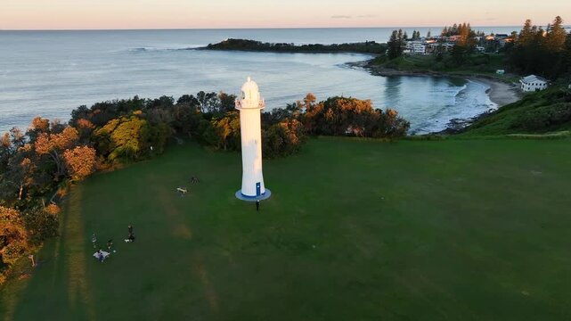Drone circles Yamba Lighthouse at sunset, gliding from north to south to reveal the breakwater and the entrance to the Clarence River, golden light reflecting on rolling waves as the coastline opens b