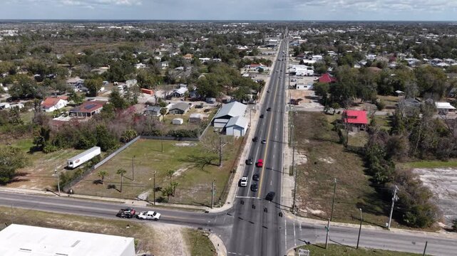 Drone orbit over long straight highway crossing suburban residential neighborhood with houses and traffic, 30A, Florida, USA