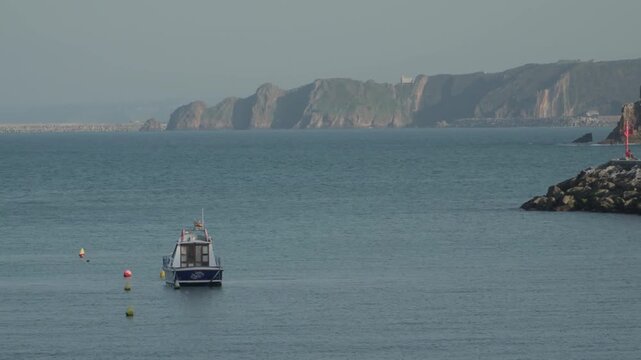 Peaceful coastal view of a small fishing boat floating on the Atlantic Ocean near Cand&aacute;s, Asturias, Spain. Distant cliffs and calm blue water create a scenic maritime landscape.