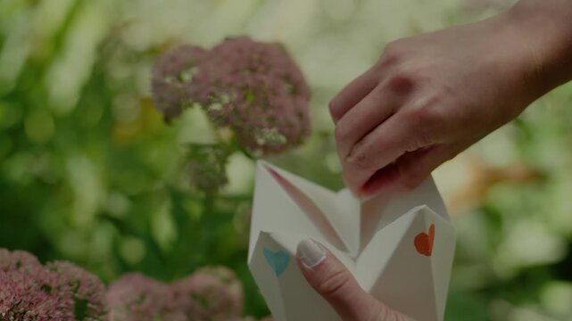 a young woman playing with a paper fortune teller aka chatterbox in lush garden