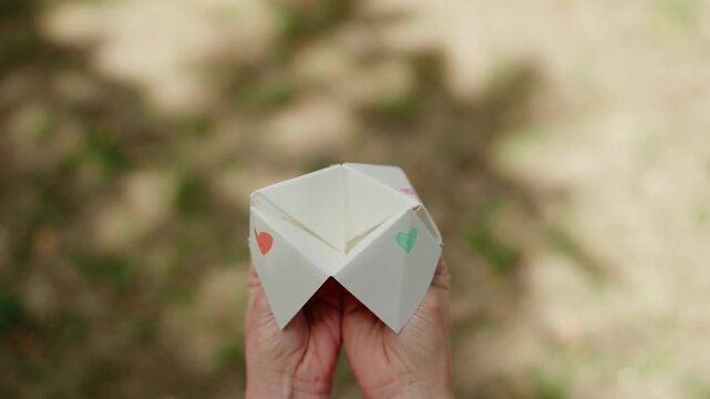 a young woman playing with a paper fortune teller aka chatterbox in lush garden reveals support