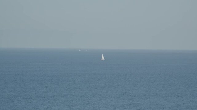 Minimalist seascape with a single white sailboat sailing across the Atlantic Ocean horizon near Cand&aacute;s, Asturias, Spain. Calm blue water and open sky create a peaceful maritime landscape.