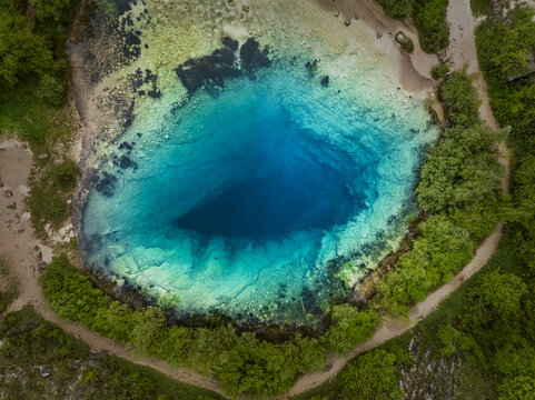 Aerial view of the Dragon Eye Earth Hole, a clear and deep turquoise pool surrounded by lush green trees, Zman, Croatia.