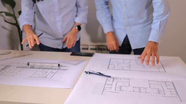 Two architects discussing architectural blueprints and floor plans for a new building project while working together on a desk in their modern office with drafting tools