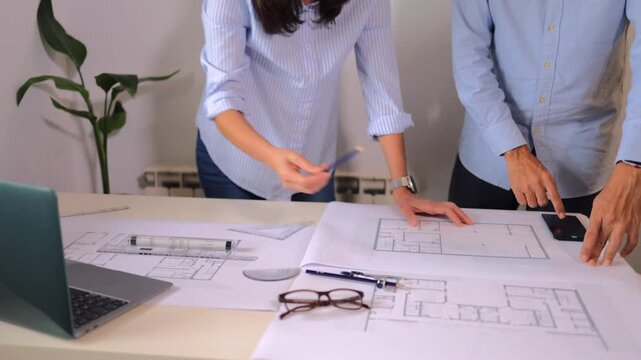 Two architects discussing architectural blueprints and floor plans on a desk, a woman and a man working together on a construction design project in their office