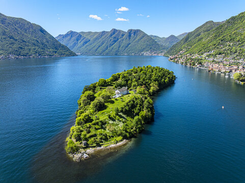 Aerial view of Isola di Loreto, a jewel of green and stone amidst the azure waters, reflecting the surrounding mountains, Domaso, Lombardy, Italy.